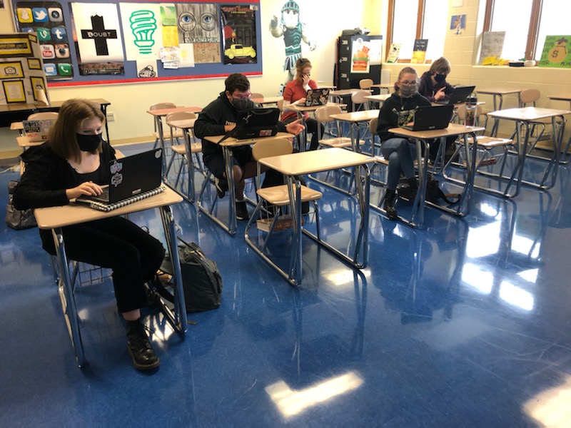 students sitting socially distanced in masks in a class room